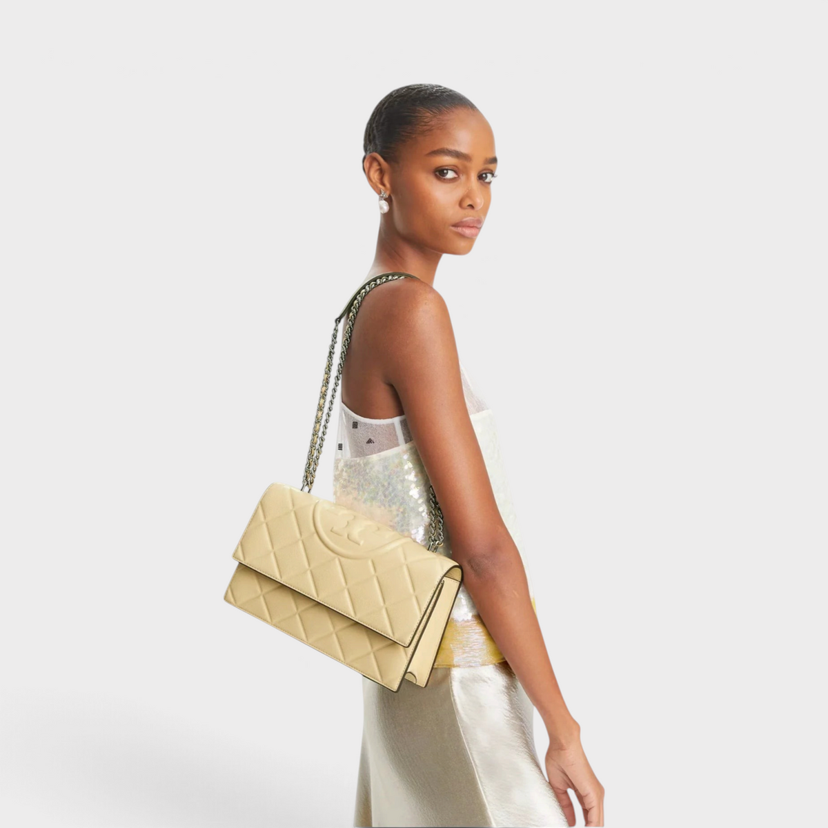 Model wearing a vanilla beige quilted leather Fleming shoulder bag by Supplied Fashion with a chain strap.
