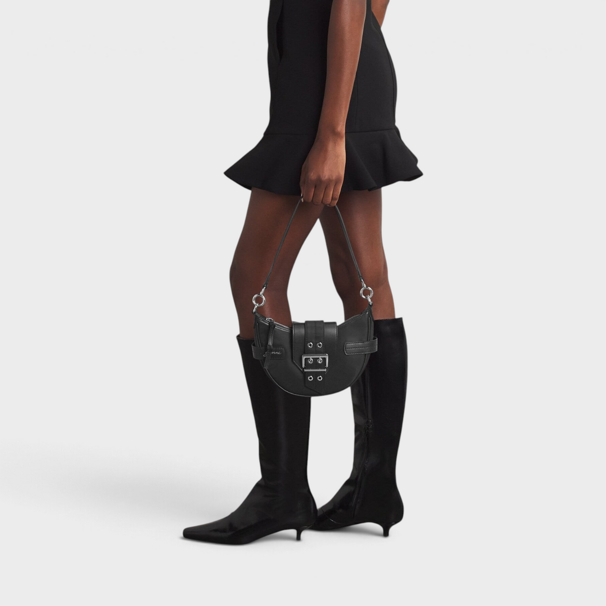 Supplied Fashion Ganni Small Bucky black cross-body bag with silver buckle detail held by a model in a black outfit.