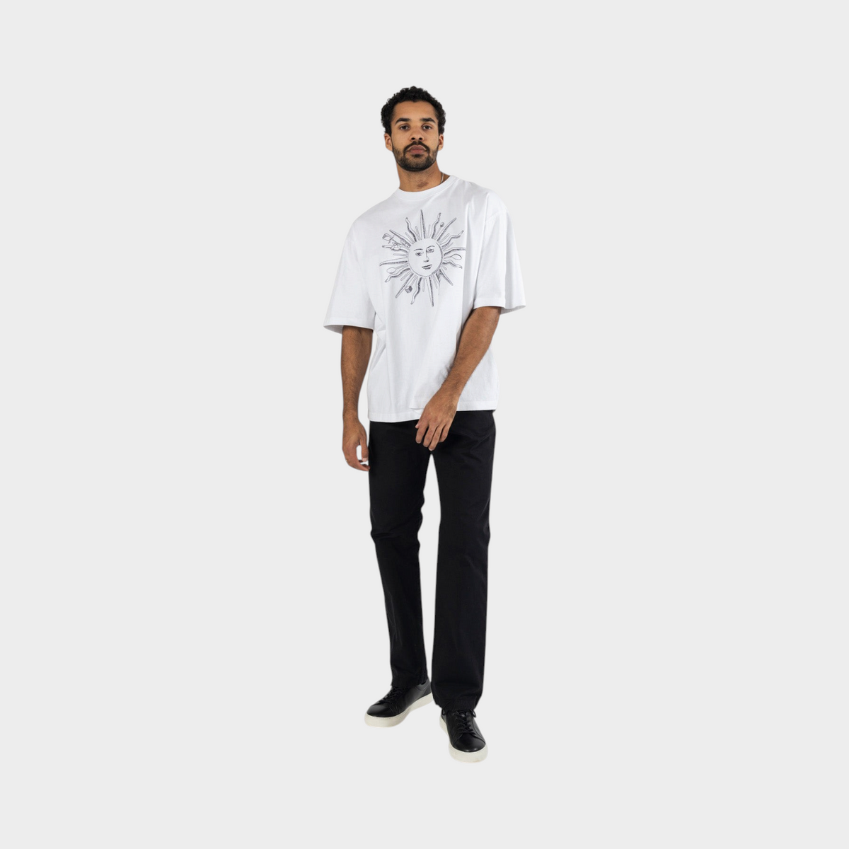 Supplied Fashion white t-shirt with black sun graphic print worn by a man with black trousers and sneakers