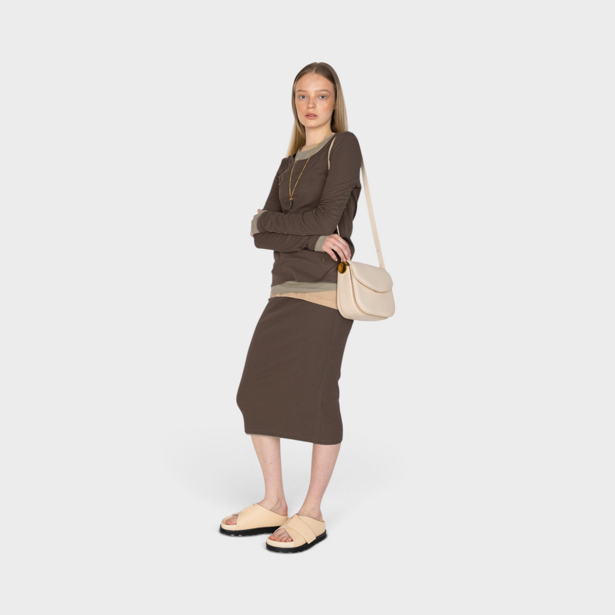 Supplied Fashion model wearing a dune beige Jil Sander leather crossbody bag with a brown skirt and matching sandals