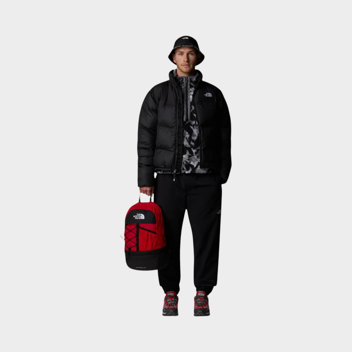 Supplied Fashion model wearing a black The North Face Saikuru puffer jacket, black joggers, and a red backpack.