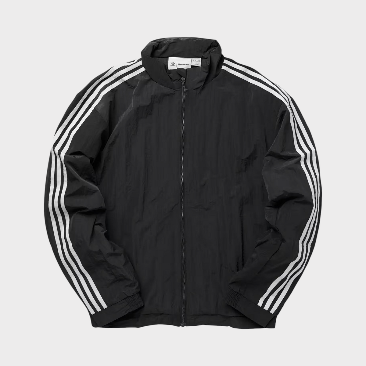 Supplied Fashion adidas Pharrell Williams black track jacket with white three-stripe detailing and zip-up front.