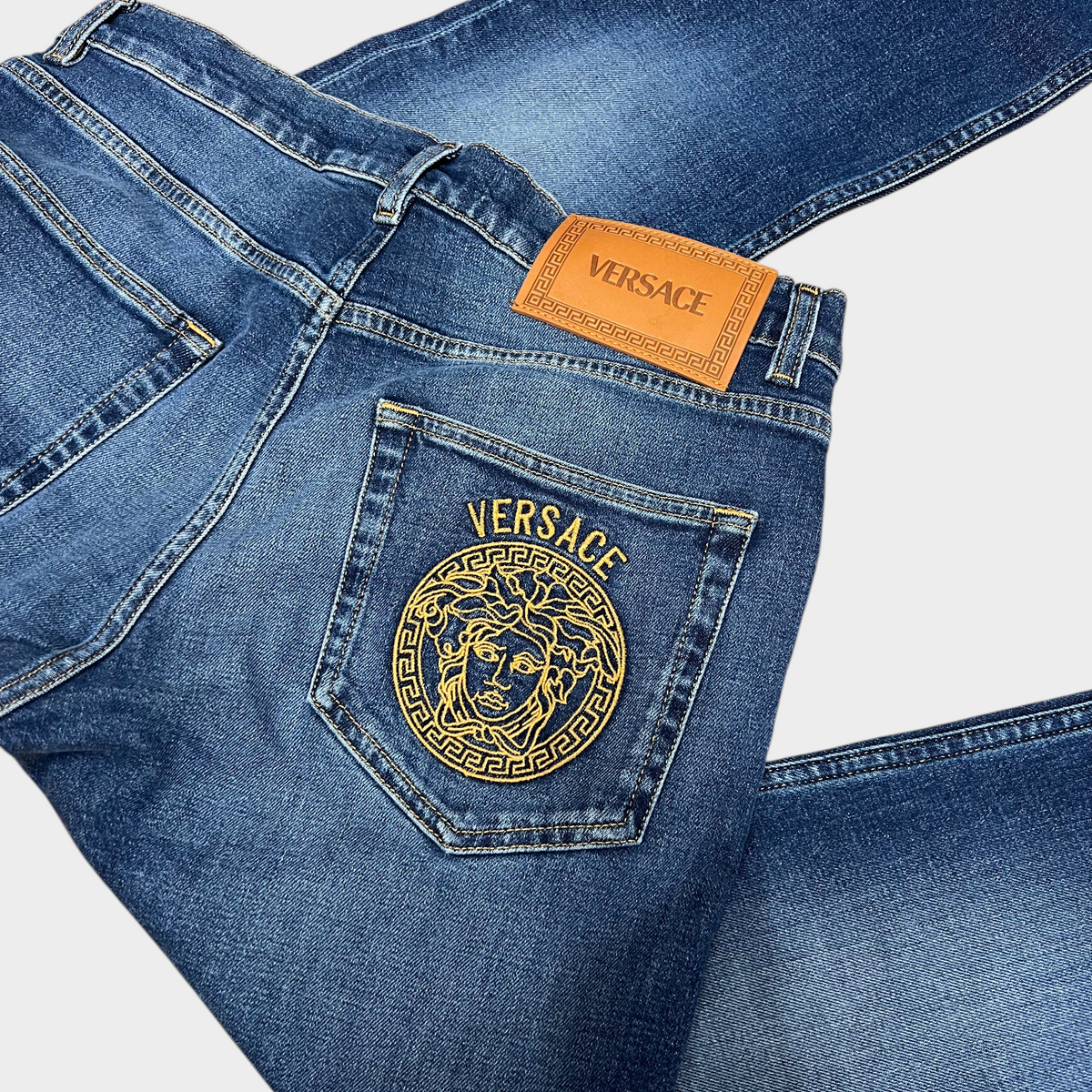 Supplied Fashion Versace Taylor blue denim jeans featuring a gold Medusa head embroidery on the back pocket.