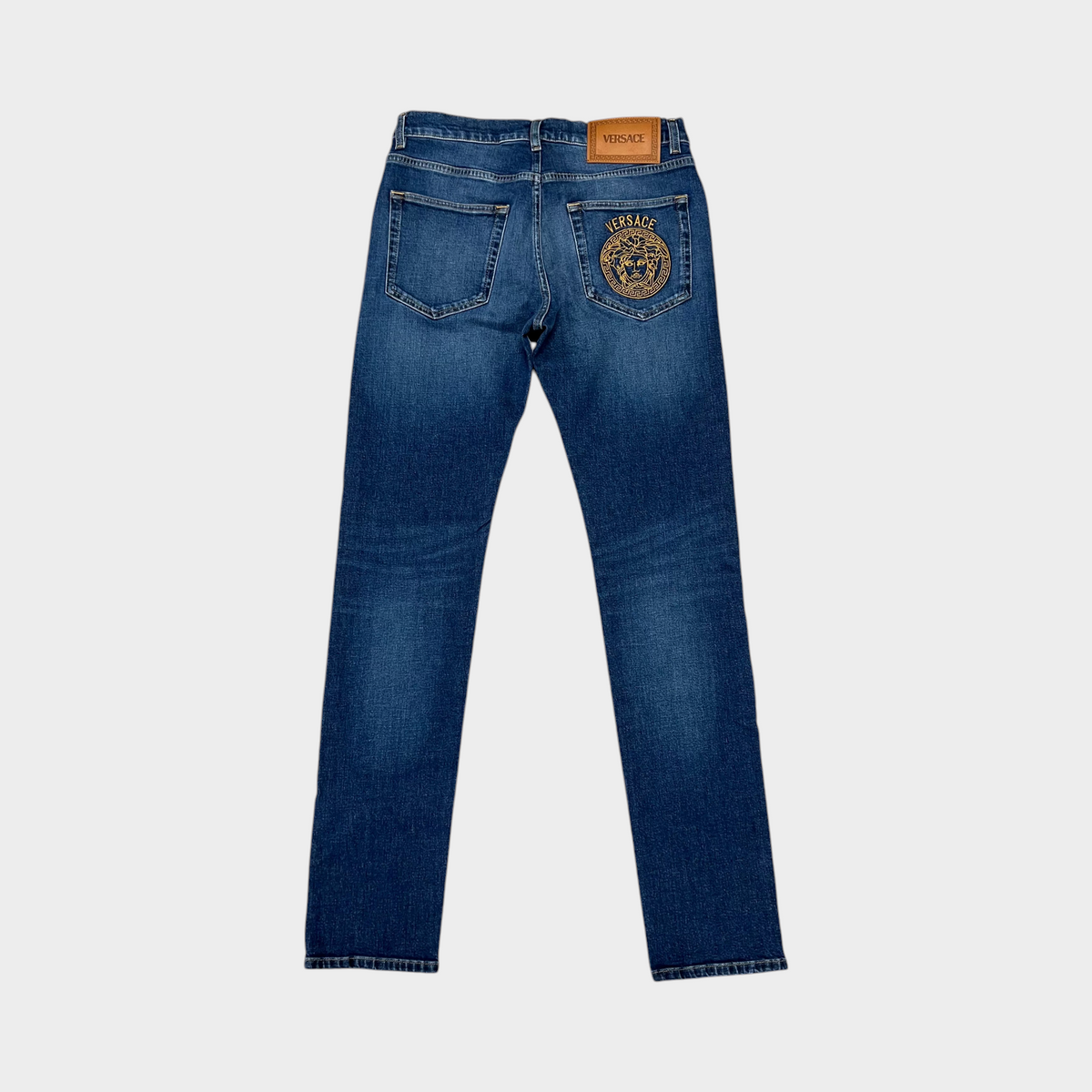 Supplied Fashion blue denim Versace Taylor jeans featuring a signature gold Medusa head motif on the back pocket.