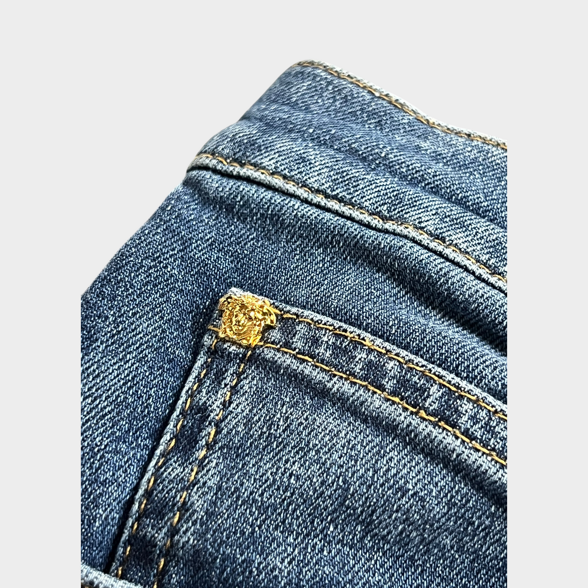 Supplied Fashion blue denim jeans featuring a gold Medusa head embellishment on the back pocket with contrast stitching
