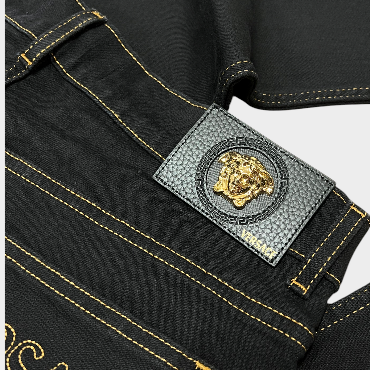 Supplied Fashion black stretch denim jeans featuring a gold Medusa head motif on a leather back patch with gold stitching