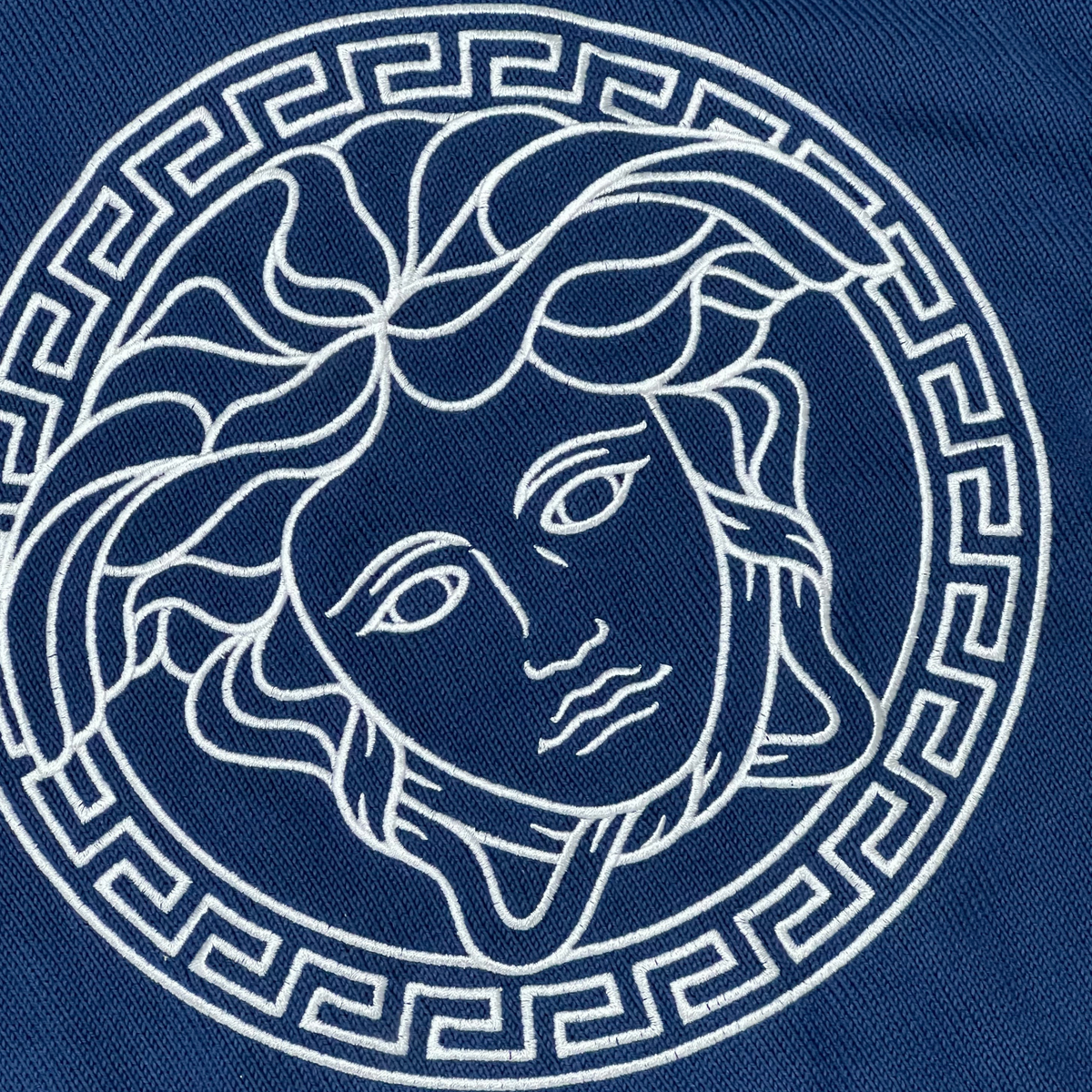 Supplied Fashion blue knit sweater featuring a detailed Medusa head embroidery with a Greek key border design.