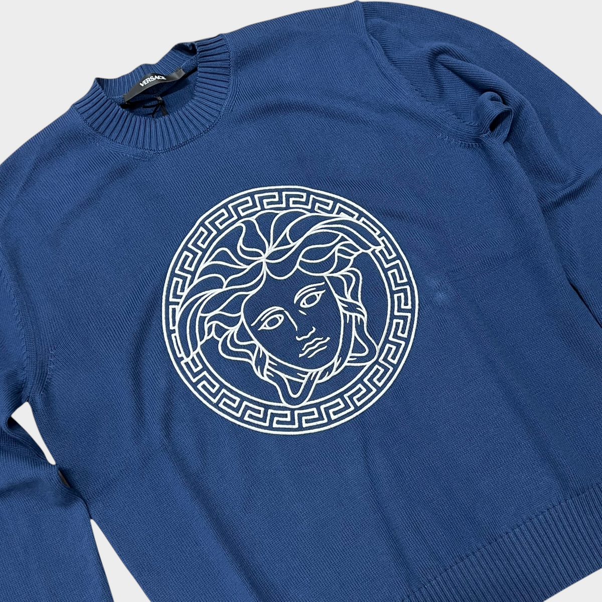 Supplied Fashion blue knit sweater featuring a white embroidered Medusa head logo and classic crew neckline.