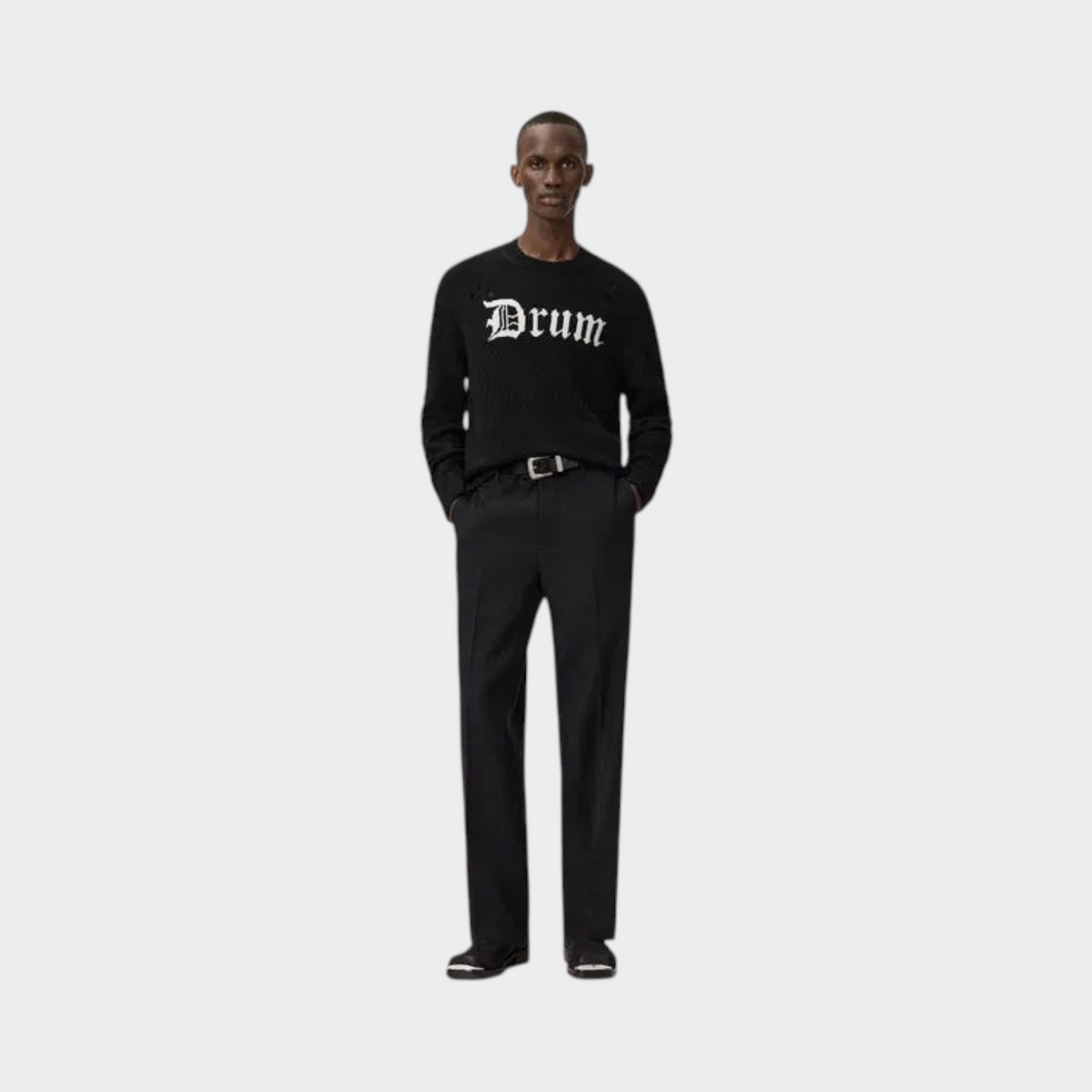 Model wearing a black Supplied Fashion Drum jacquard knit jumper with white gothic lettering and tailored trousers.