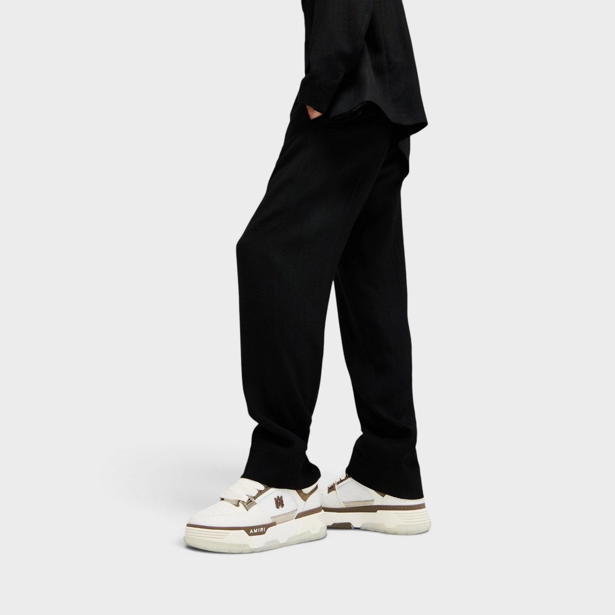 Supplied Fashion AMIRI MA-1 white and brown leather sneakers worn with black trousers in a side profile view