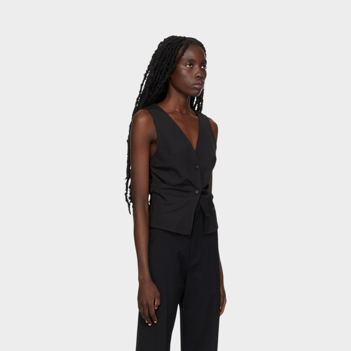 Model wearing a sleek black tailored gilet by Supplied Fashion, featuring a V-neck and button-front closure.