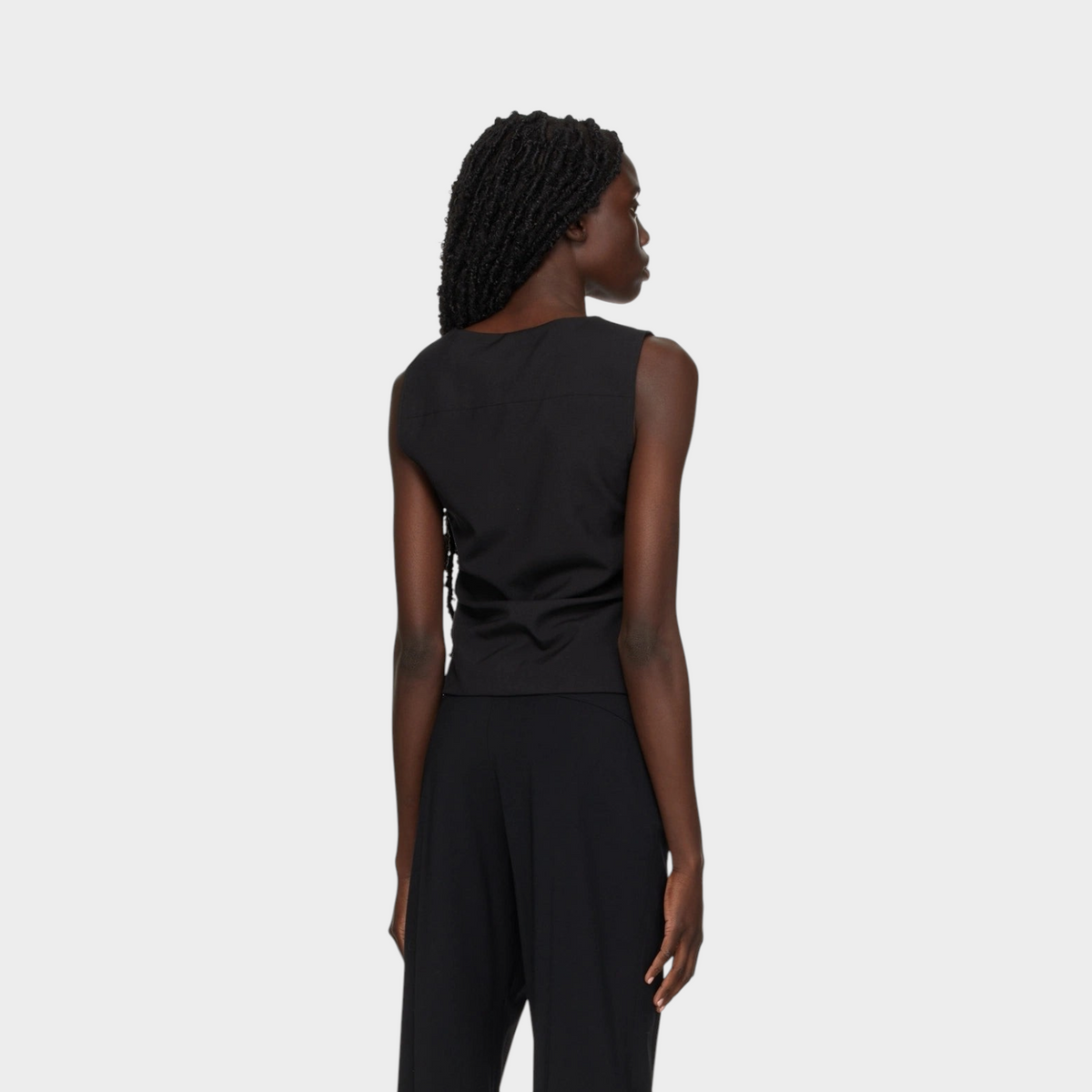 Model wearing a sleek black tailored gilet by Supplied Fashion, viewed from the back against a neutral background.