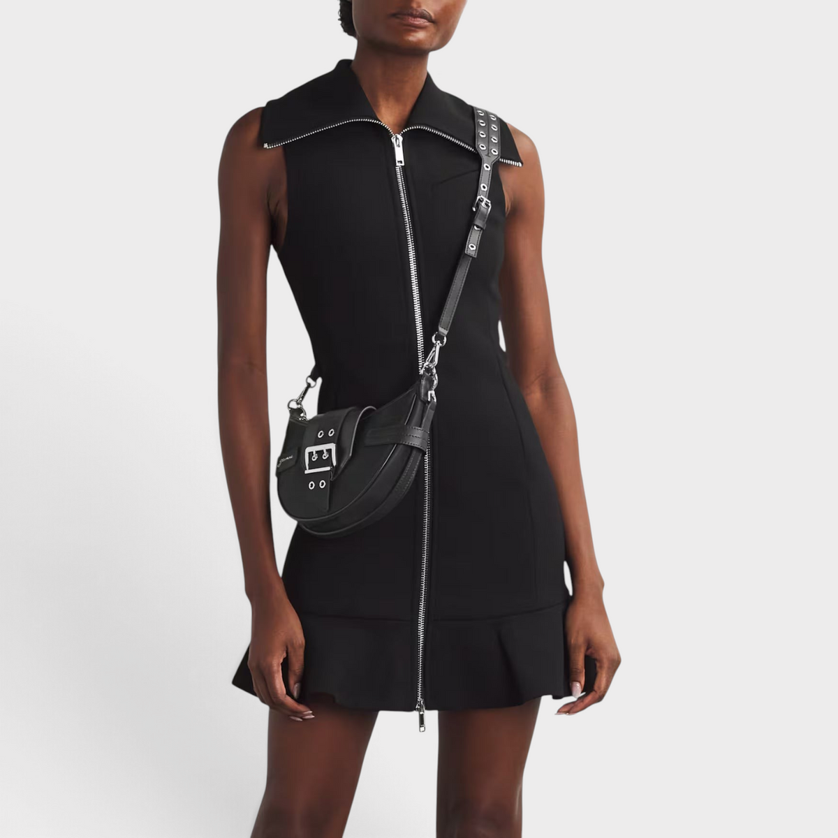 Supplied Fashion black Ganni Small Bucky cross-body bag with silver buckle detail worn by a model in a black dress.