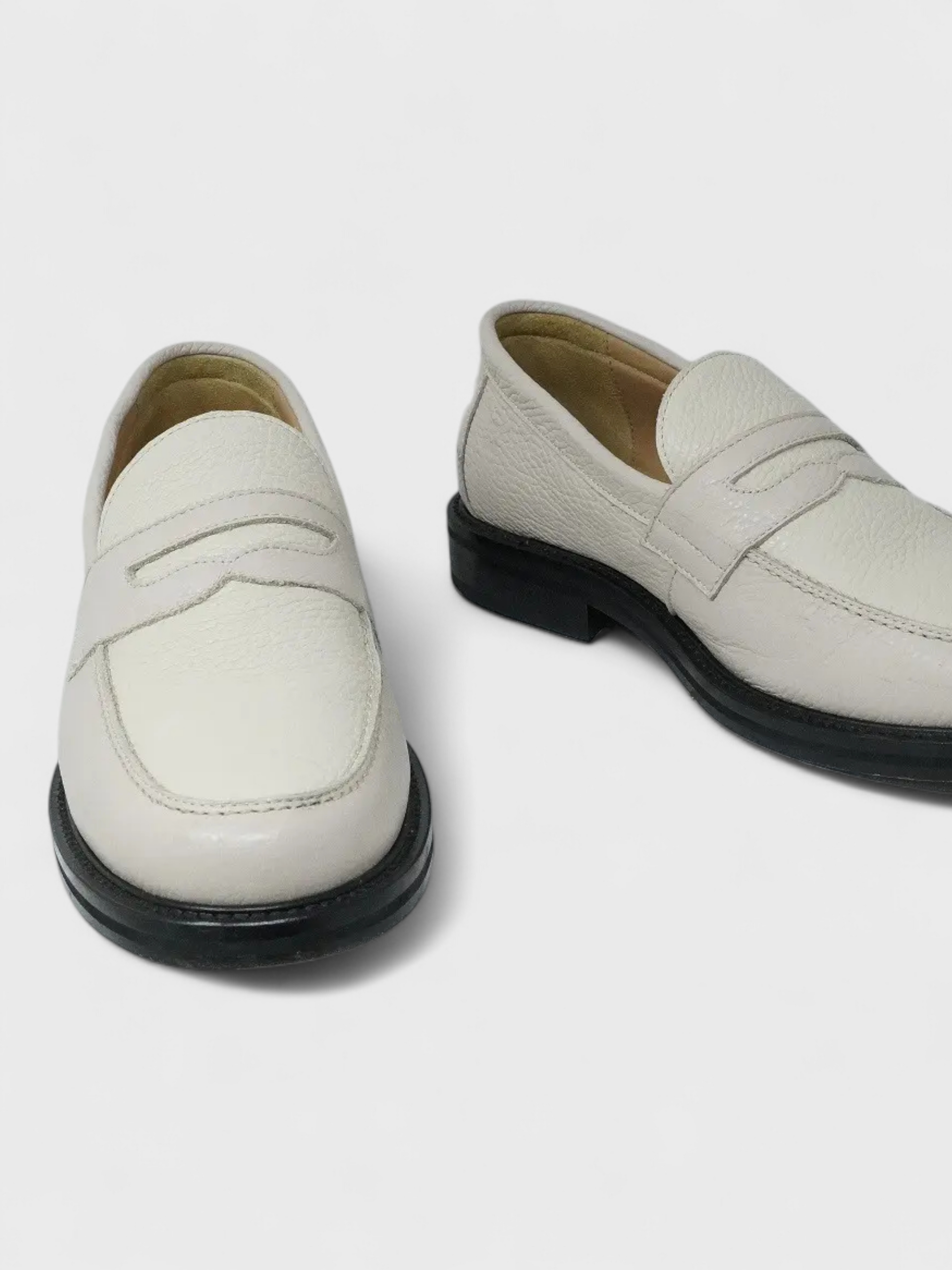 Pair of white loafers with black soles on a light gray background