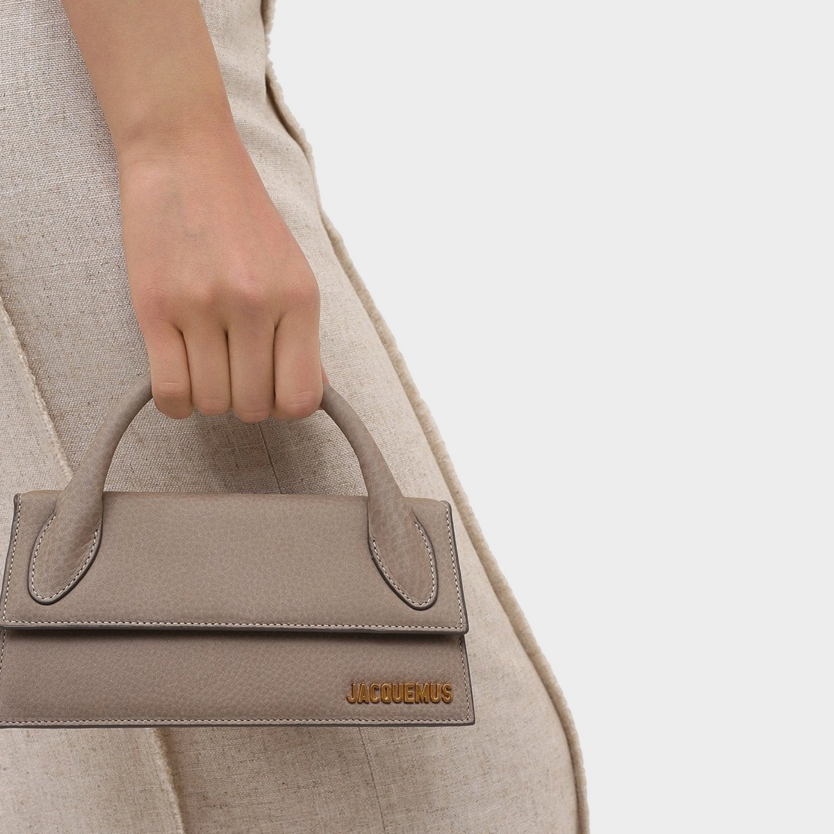 Supplied Fashion Le Chiquito Long light beige structured leather handbag held by a hand against a plain background