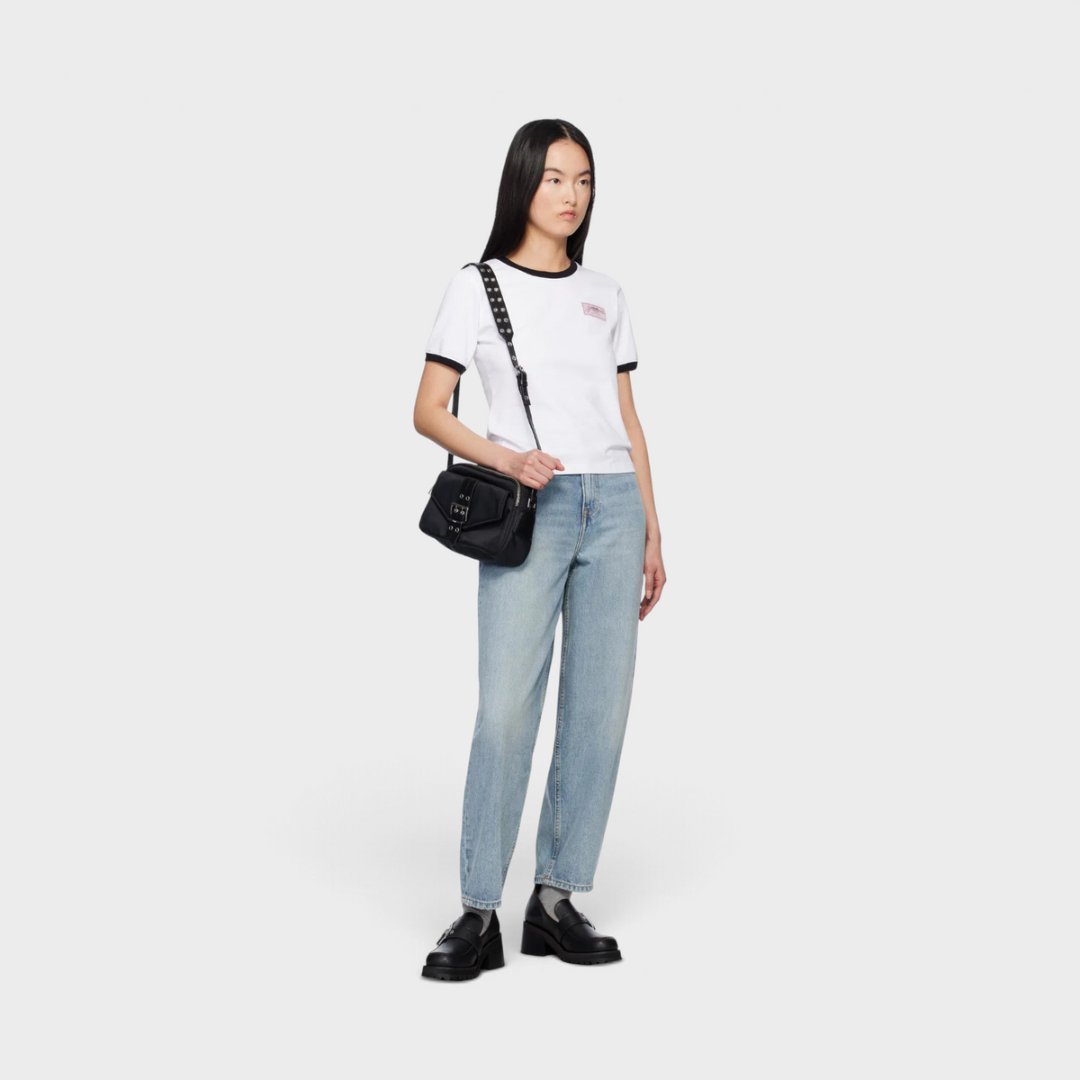 Model wearing a black Ganni Bucky camera bag crossbody with a white t-shirt, light wash jeans, and black loafers.