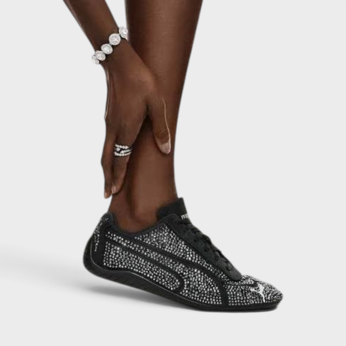 Supplied Fashion Puma X Swarovski Speedcat black sneaker with crystal embellishments on a model's foot