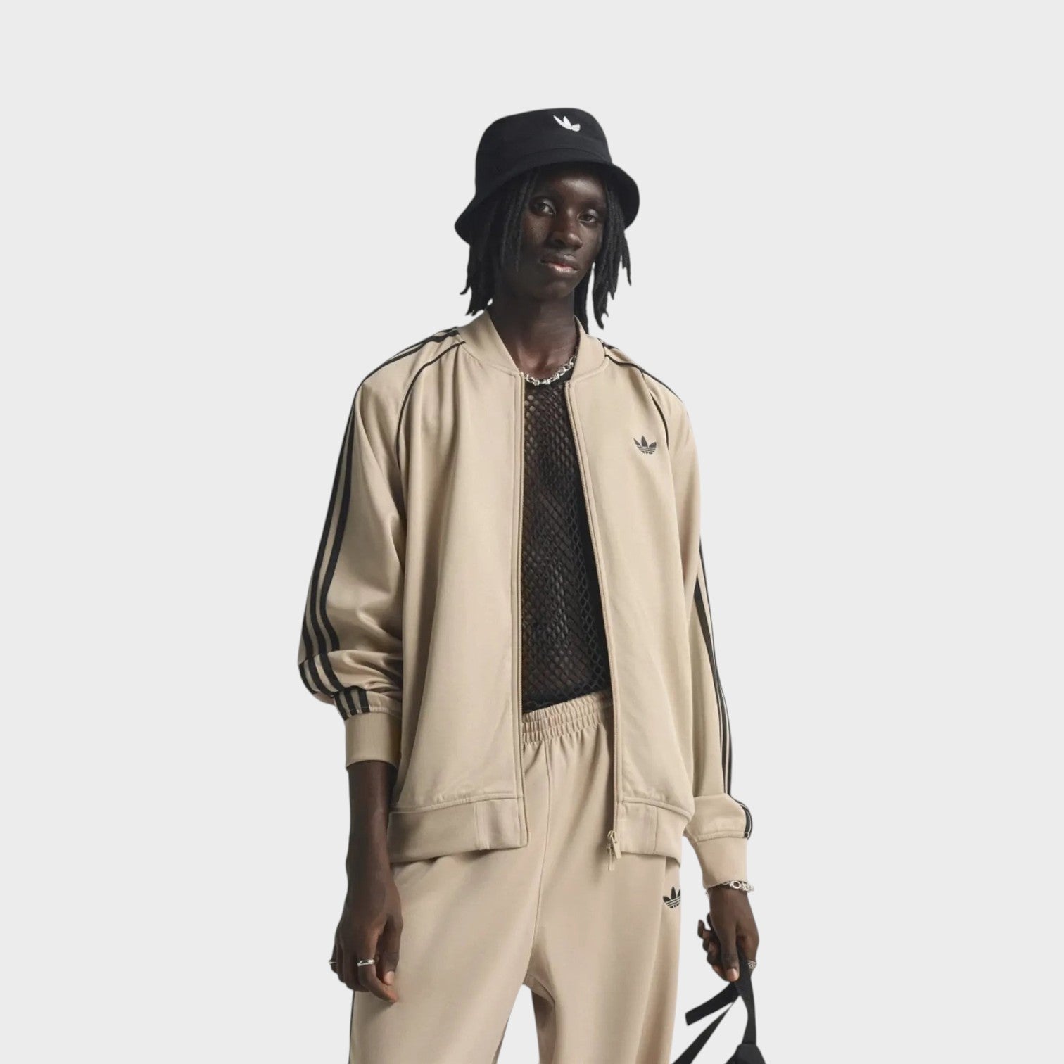 Supplied Fashion beige and black loose fit track top with iconic three stripes and zip-up front on a male model