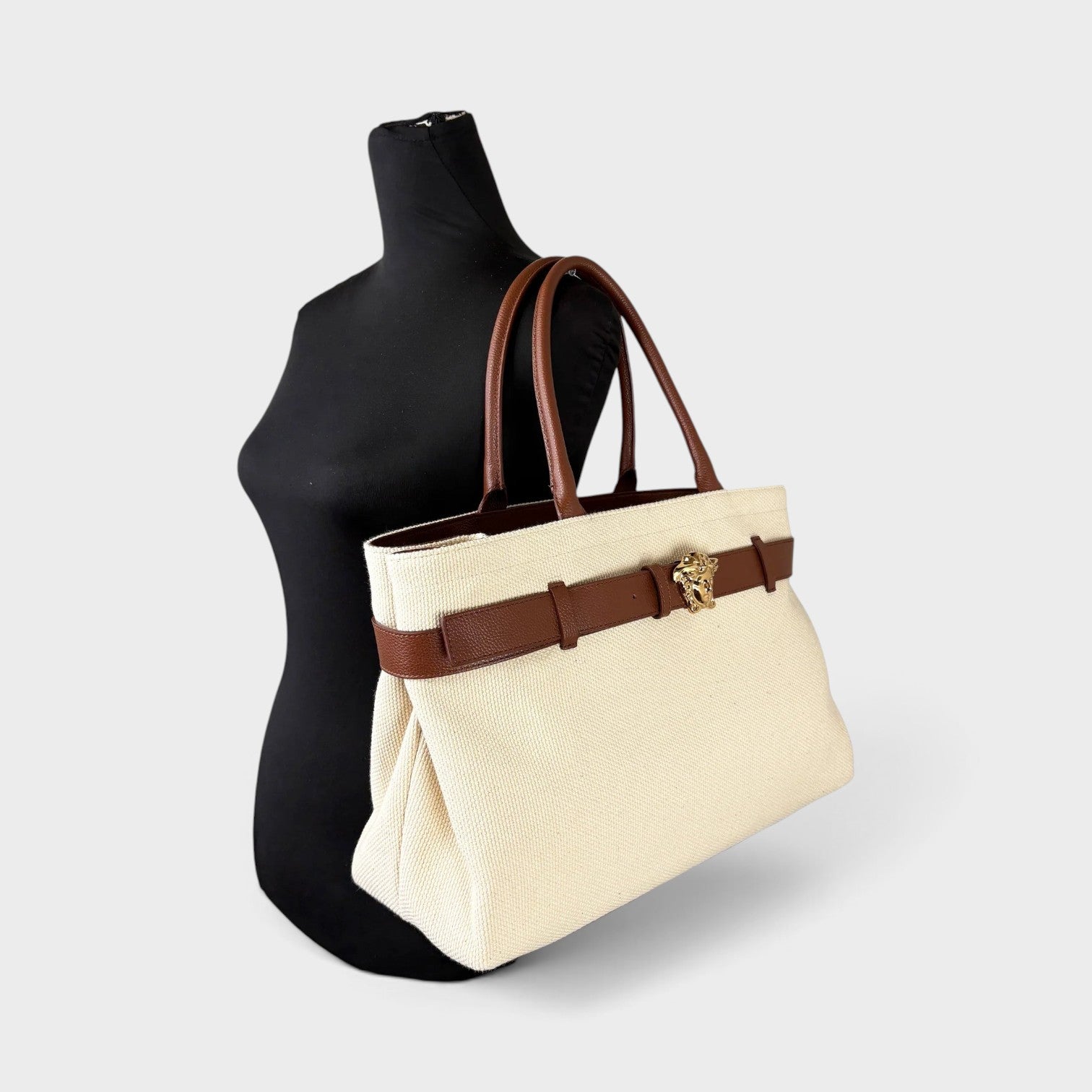 Supplied Fashion beige canvas tote bag with brown leather trim and gold Medusa head belt detail on a mannequin