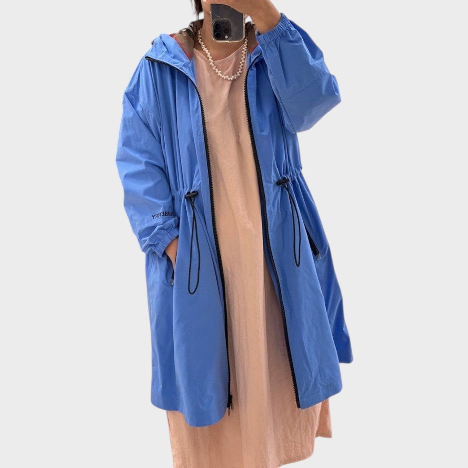 Supplied Fashion Birley long blue hooded jacket with drawstring waist and black zipper detail worn over a peach dress