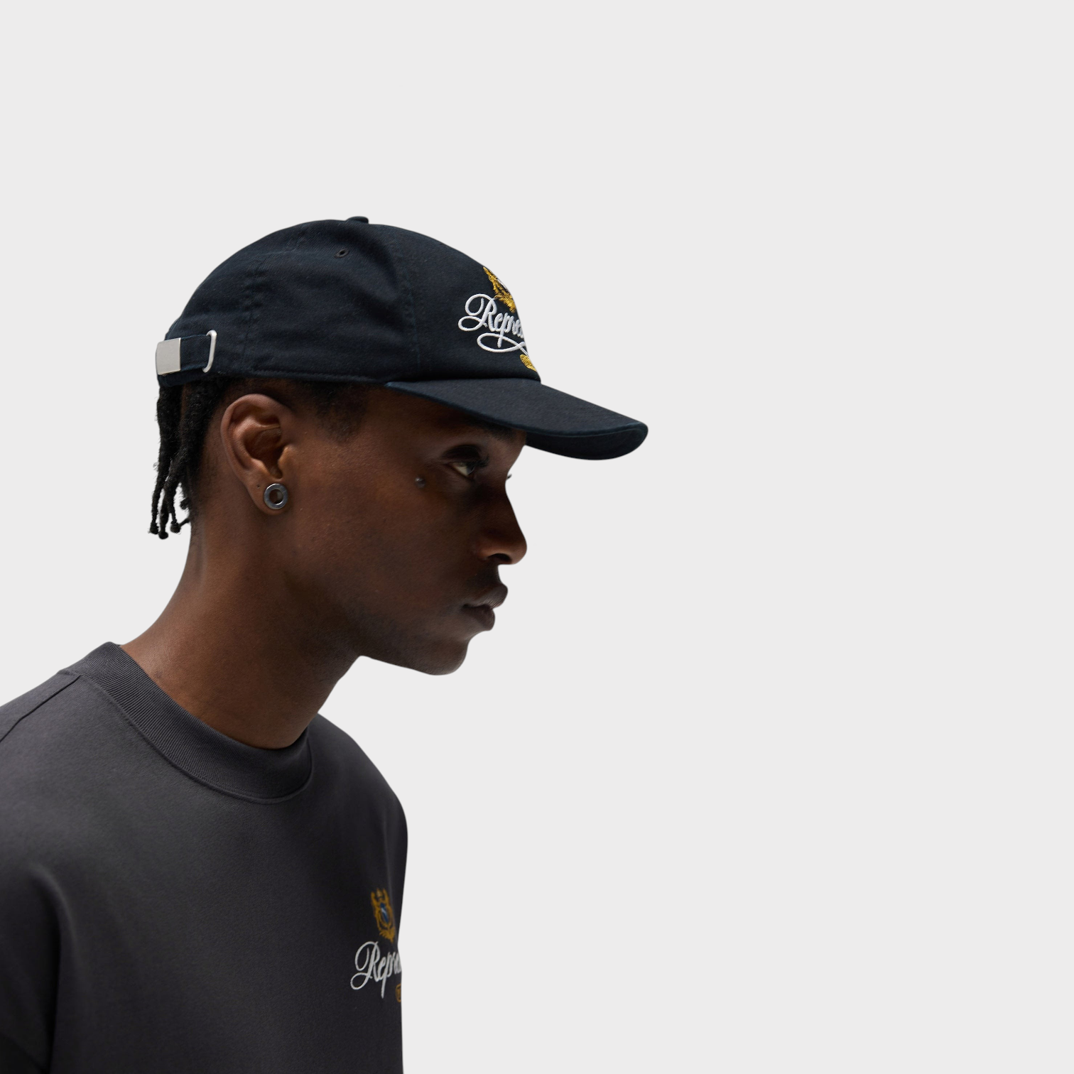 Supplied Fashion black baseball cap with embroidered logo crest worn by a man in profile view