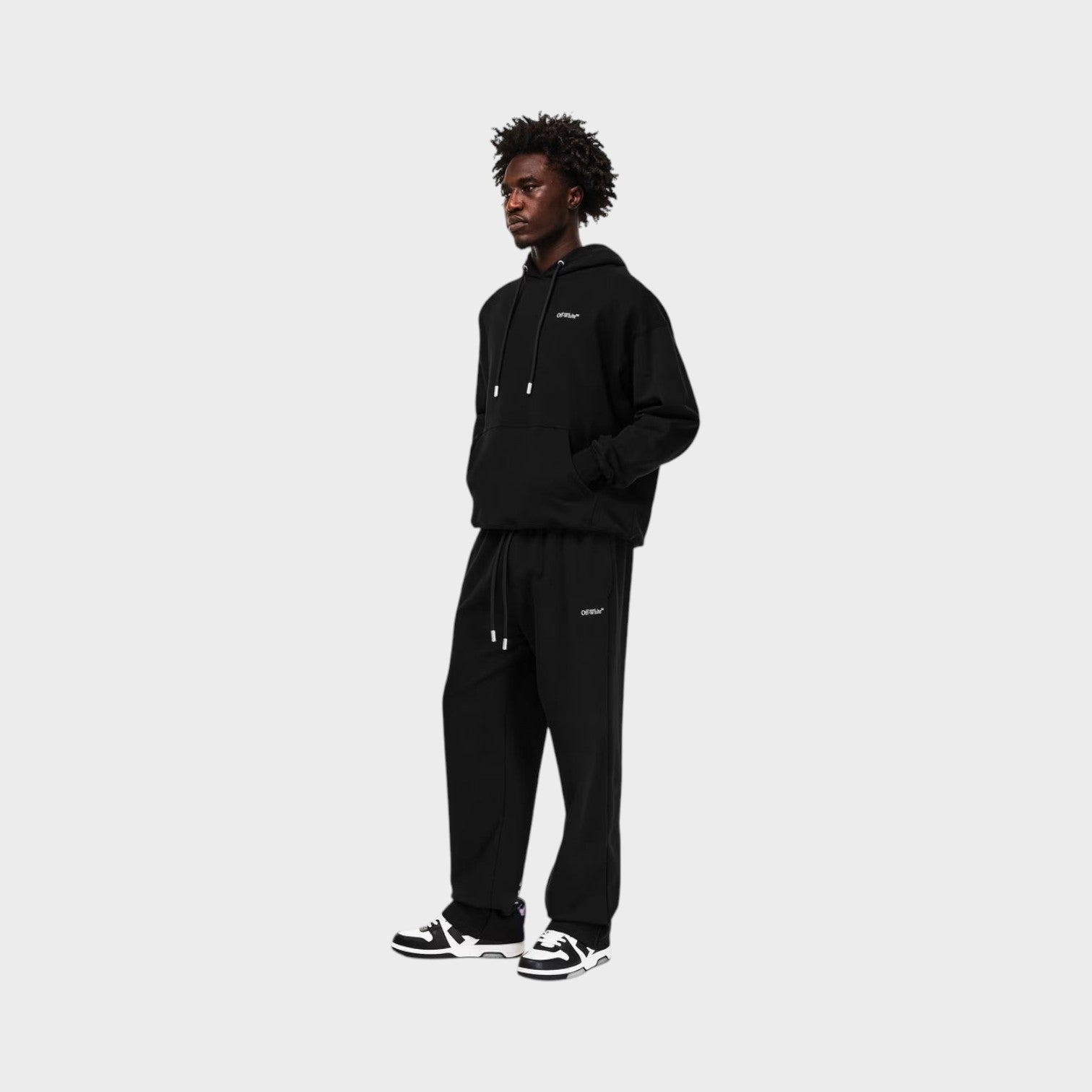 Supplied Fashion model wearing black heavyweight fleece sweatpants with signature arrow branding and closed hems