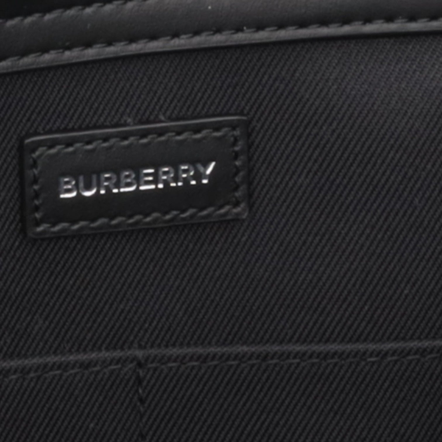 Supplied Fashion Burberry Ormond bag interior featuring a black canvas lining and a branded leather logo patch.