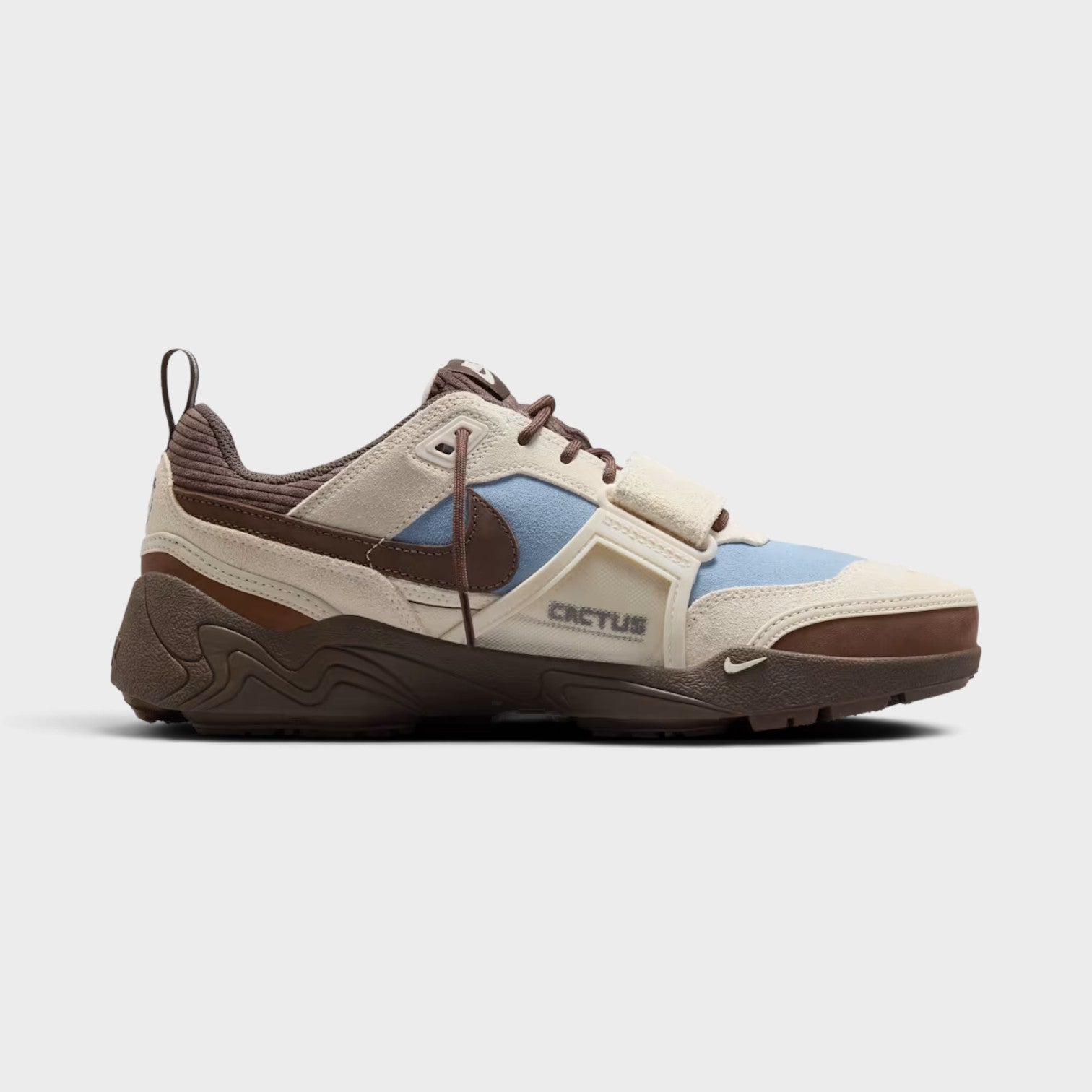 Supplied Fashion Cactus Jack Zoom Field Jaxx sneaker in pale ivory, blue, and brown with a midfoot strap and branding.