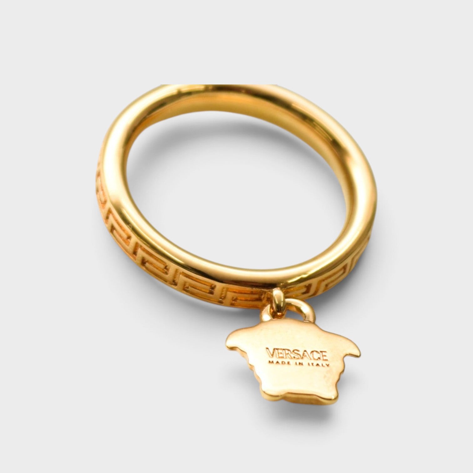Supplied Fashion gold ring featuring a Greca pattern band and a dangling Medusa head charm with Versace branding.