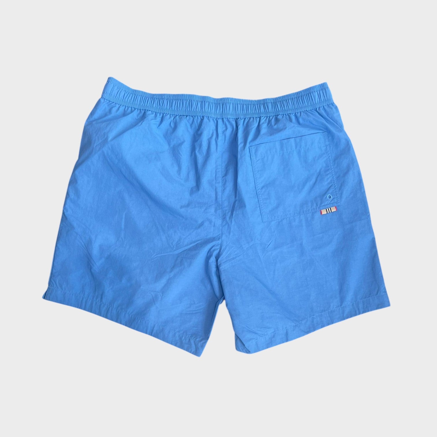 Supplied Fashion periwinkle blue nylon swim shorts with an elastic waistband and a back pocket featuring logo detail.