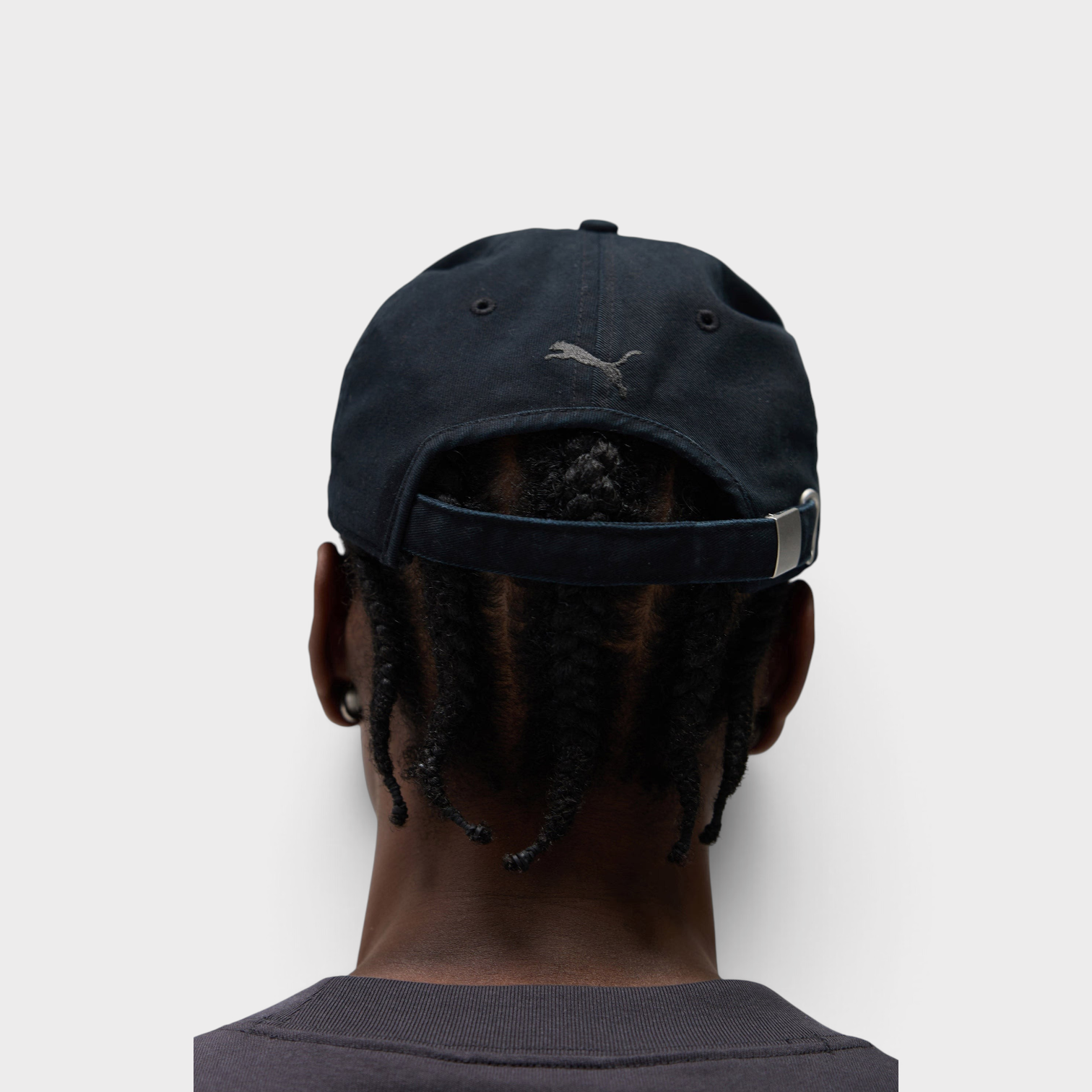 Supplied Fashion Puma black baseball cap with embroidered logo on back, worn by a person with braided hair