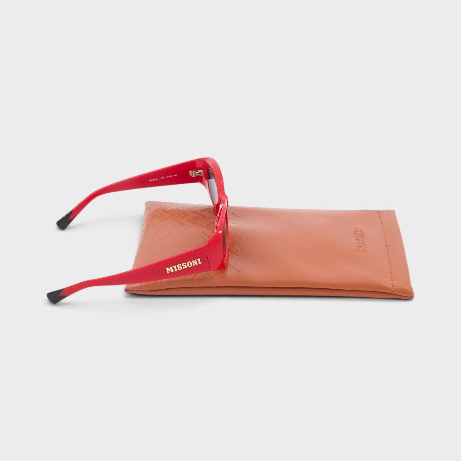 Supplied Fashion red rectangular Missoni sunglasses with logo on temple resting on a tan leather protective case.