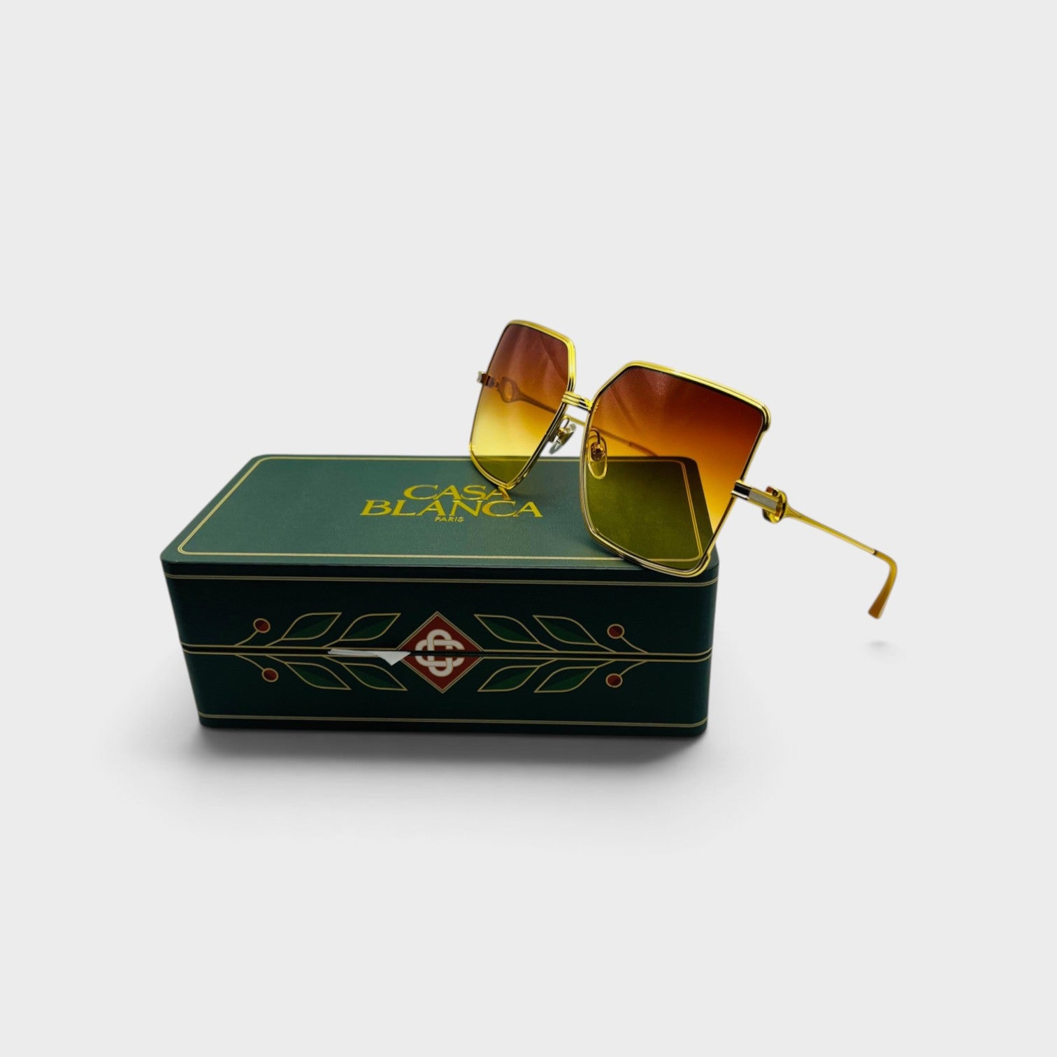 Supplied Fashion square stainless steel sunglasses with orange sunset gradient lenses resting on a green branded box